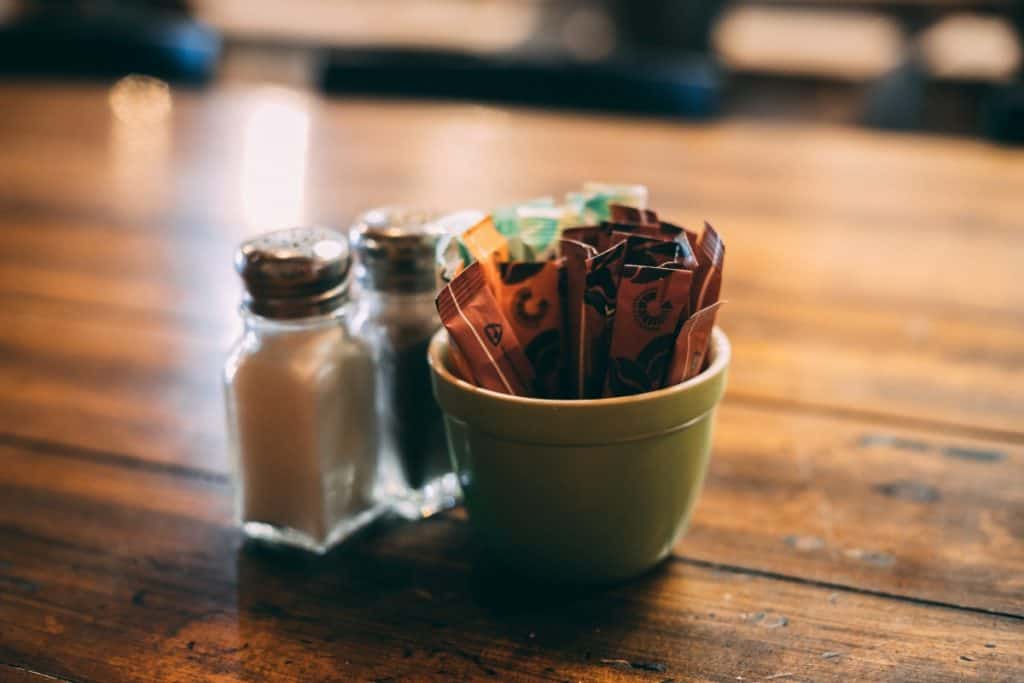 Salt and pepper shakers, a little bowl of small sugar packets on a brown wooden table
