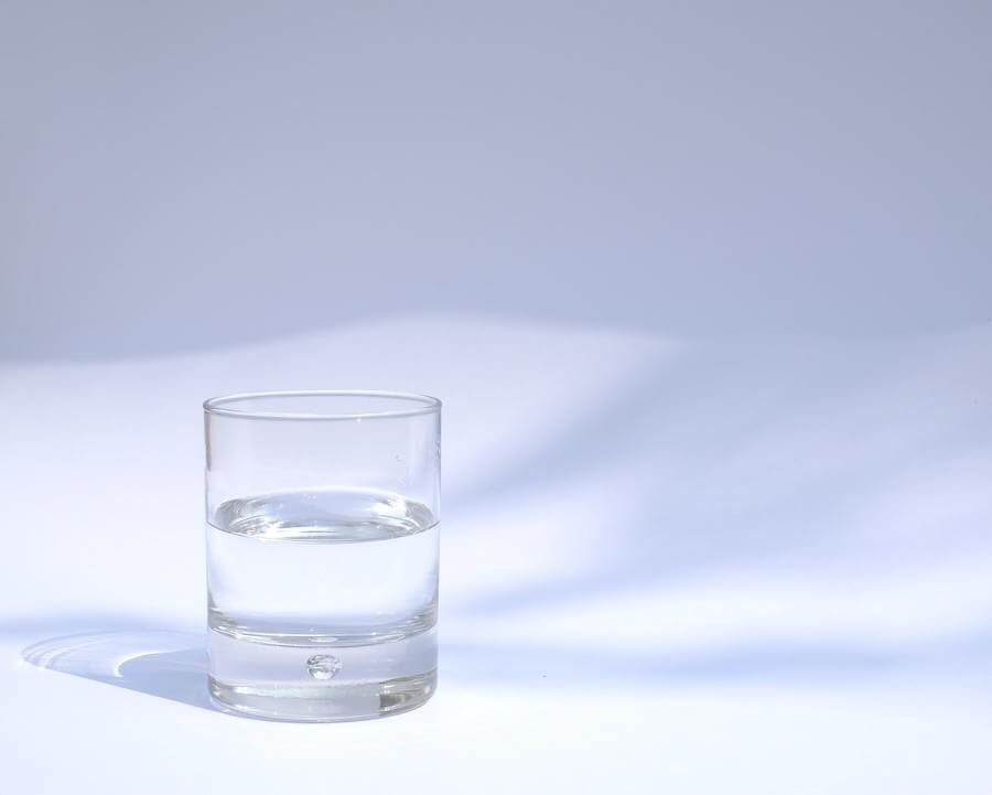 un bicchiere d'acqua riempito a metà in uno sfondo vuoto di spazio bianco