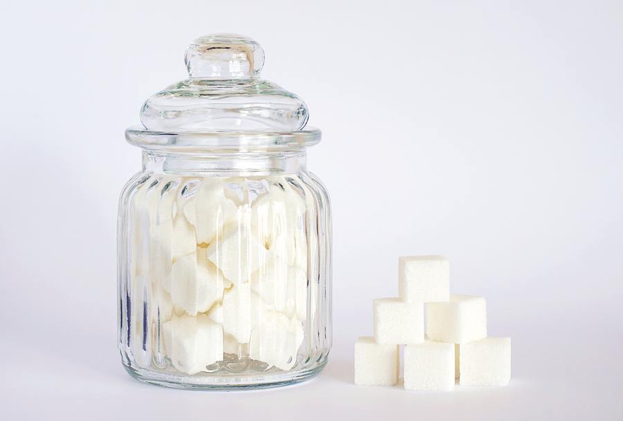 Sugar cubes in glass container with sugar cubes stacked to the site on a clear background.