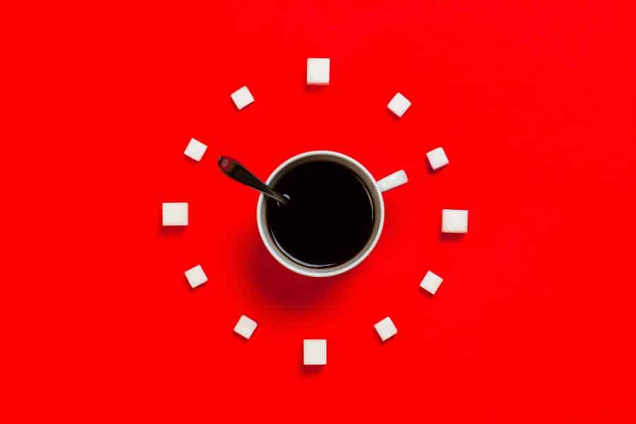 Cup of coffee in the middle of a red background surrounded by sugar cubes in a clock-like format