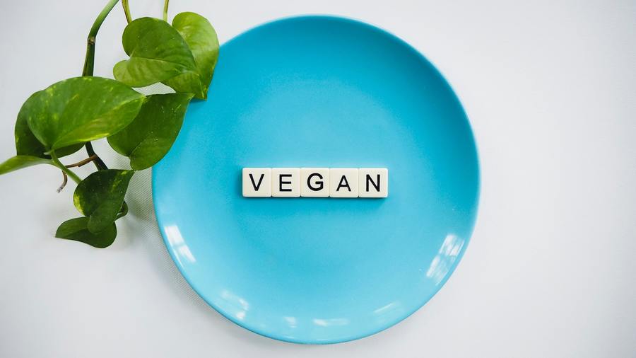 Scrabble-like tile spelling out Vegan on a cyan plate on a white background.