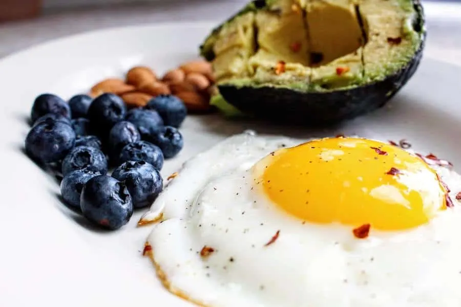 A fried egg with a side ofo blueberries, nuts and half an avocado on a plate