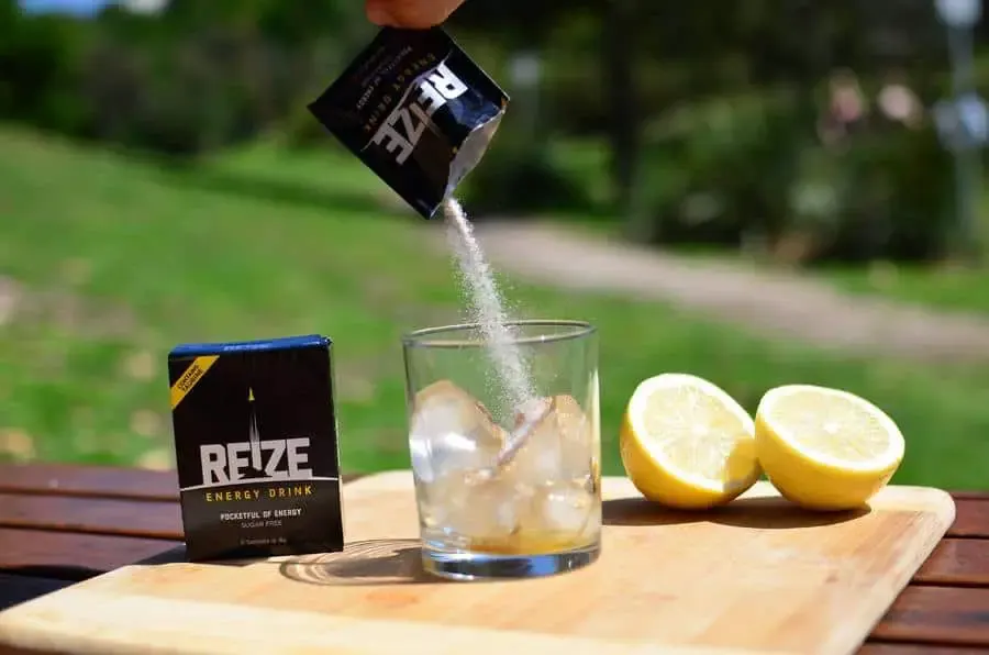 REIZE powder poured into a glass of ice with lemons in the background. 