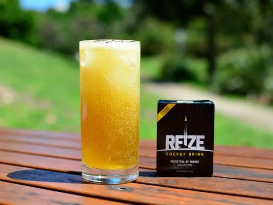 A glass of REIZE energy drink on a table with a park as backround.
