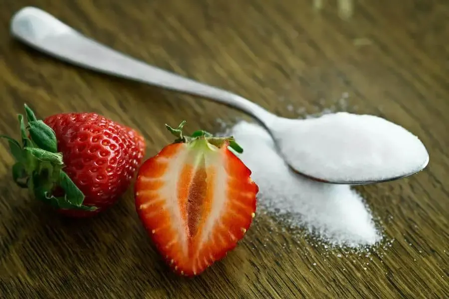A spoonful of sugar next to strawberries.