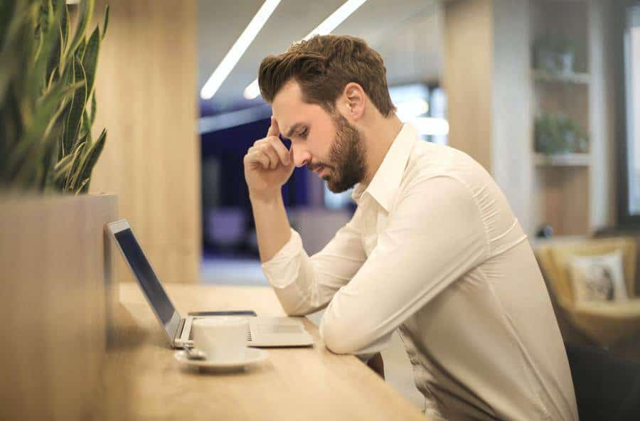 Guy thinking hard in front of a laptop and cup of coffee in front of him