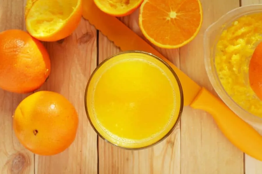 Glass of orange juice with fruit surrounding it