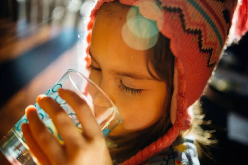A little girl is drinking a glass of water. 