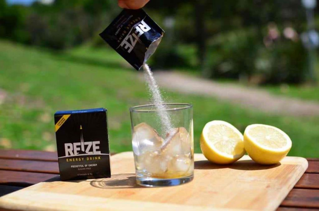A sachet of REIZE energy drink being mixed with a glass full of ice.