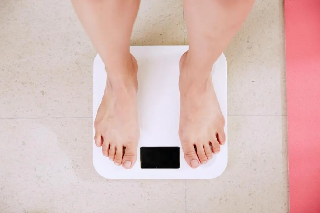 A woman stands on a weighing scale. 