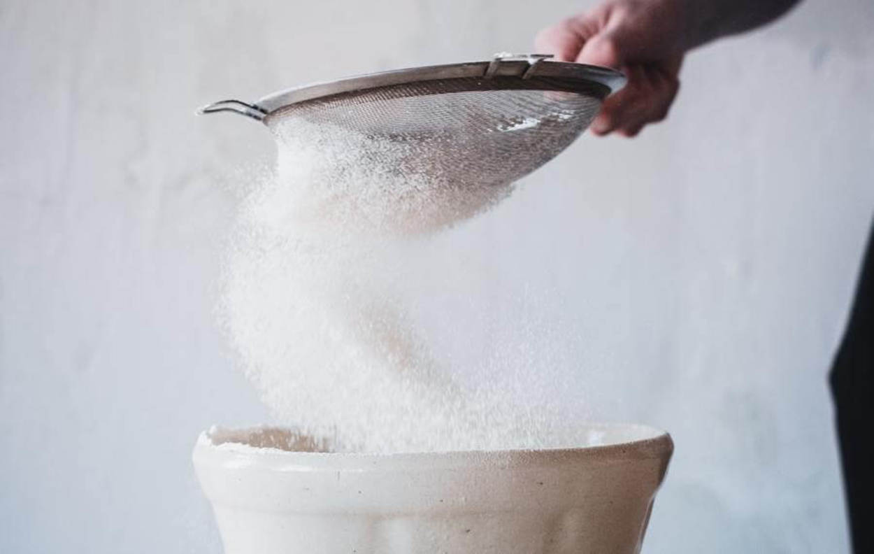 Sieving sugar into a bowl.