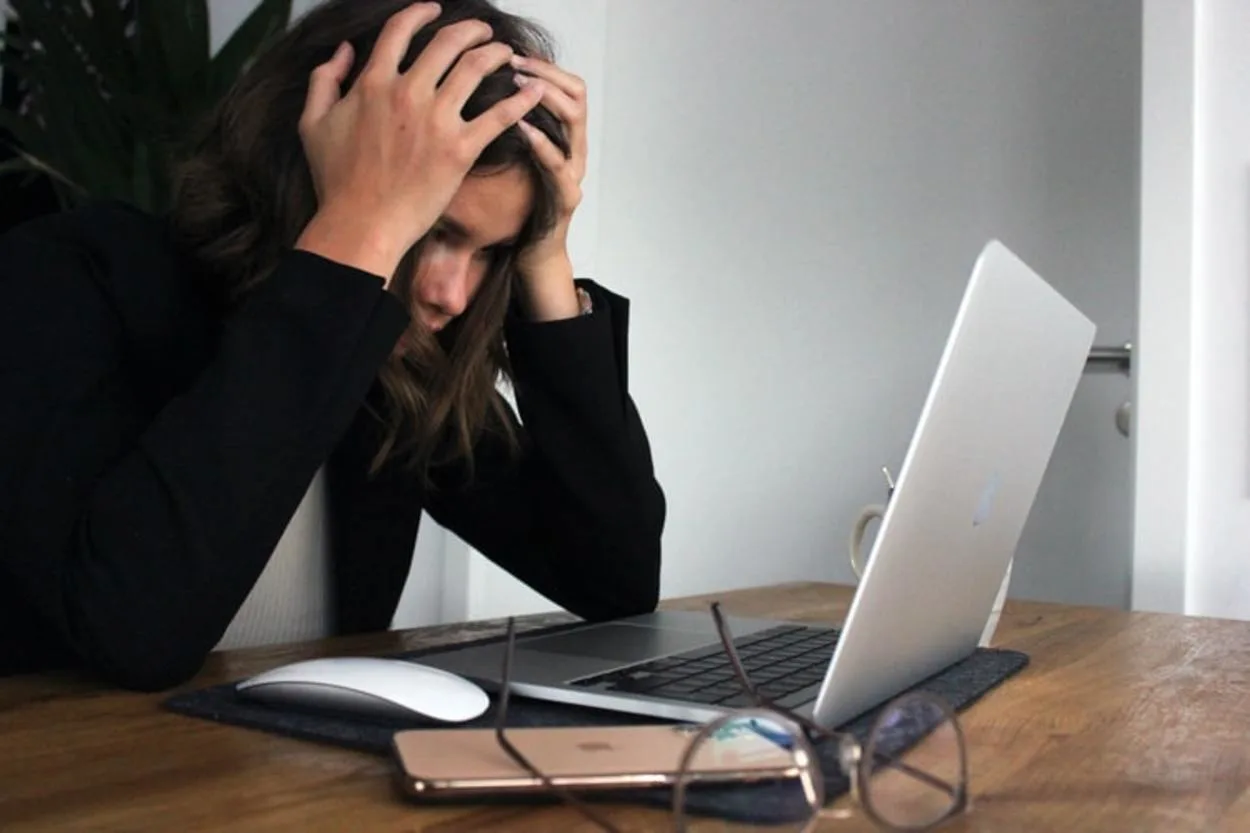 A woman holding her head while looking at her laptop screen. 