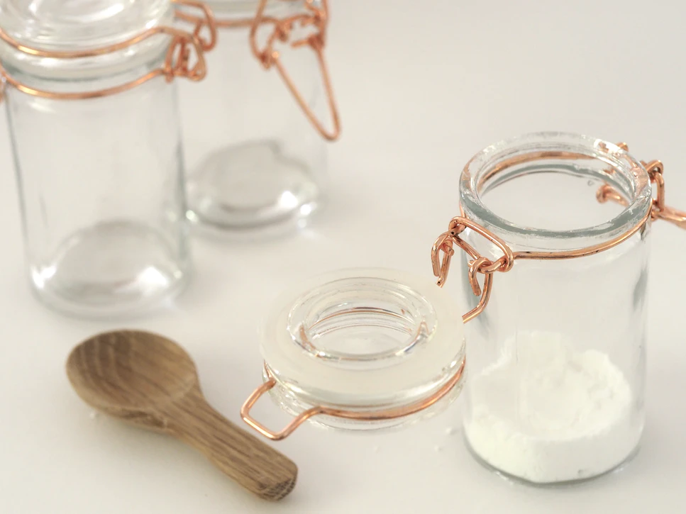 A wooden spoon beside a glass jar with sugar inside