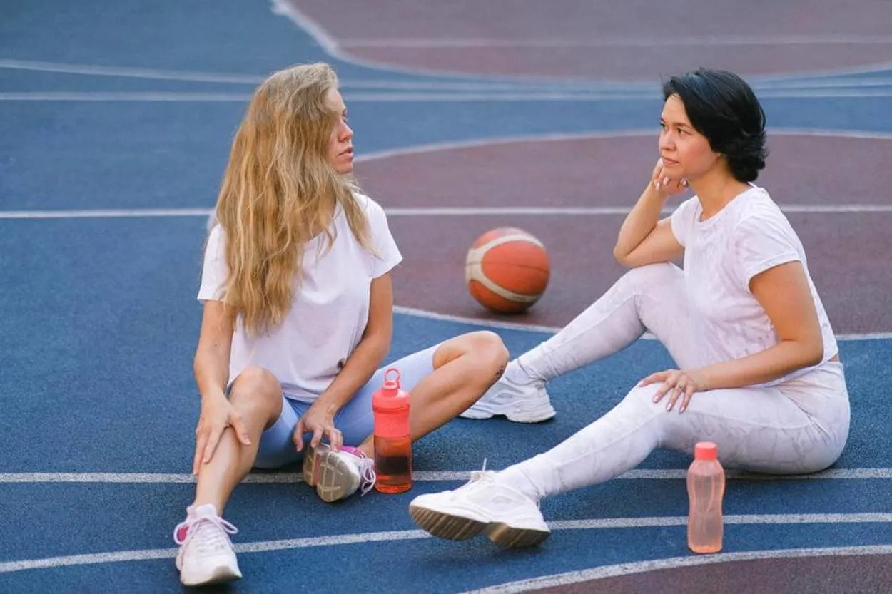 Two woman resting in the middle of a court, with their drinks. 