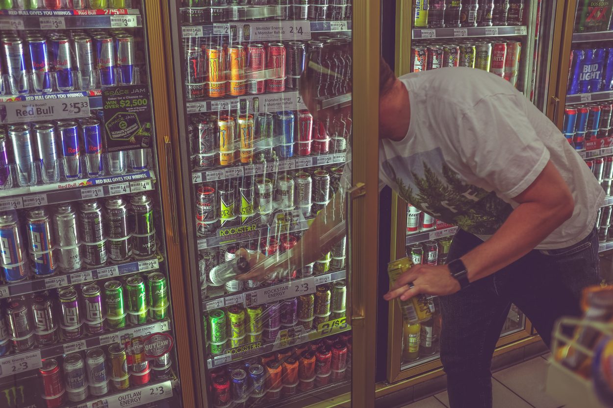 A man getting an energy drink from a fridge in a convenience store