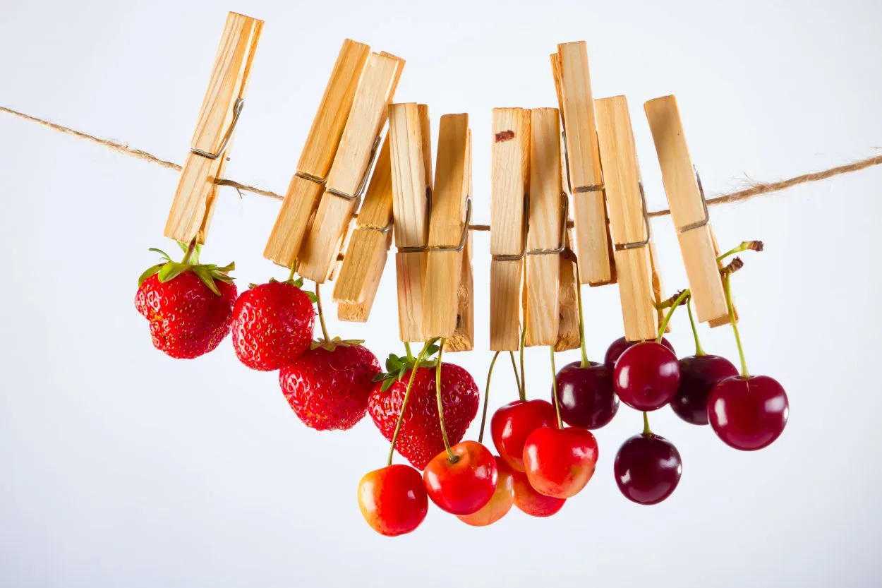 Cherries and strawberries hanging on a clothes line with the help of clothespins.