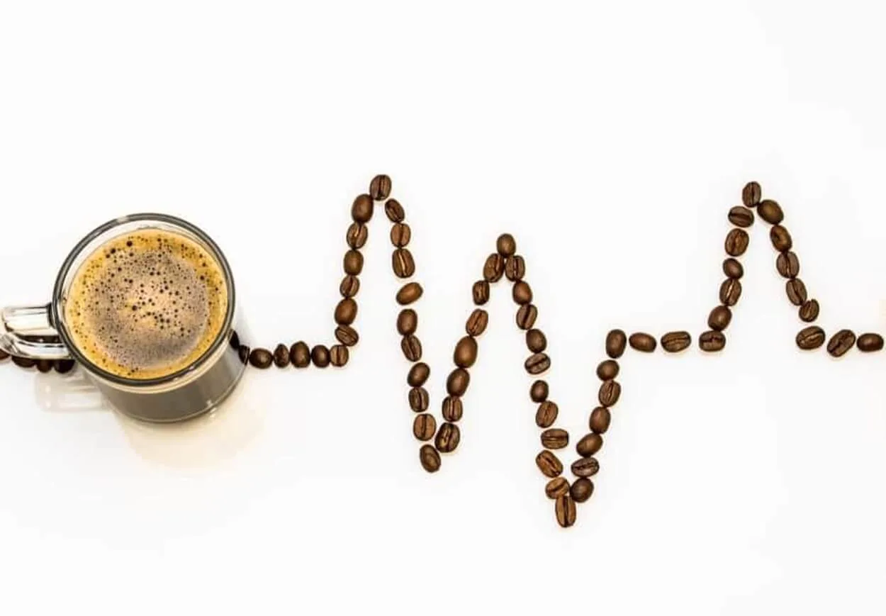 A cup of coffee and coffee beans arranged in a heart rhythm monitor.