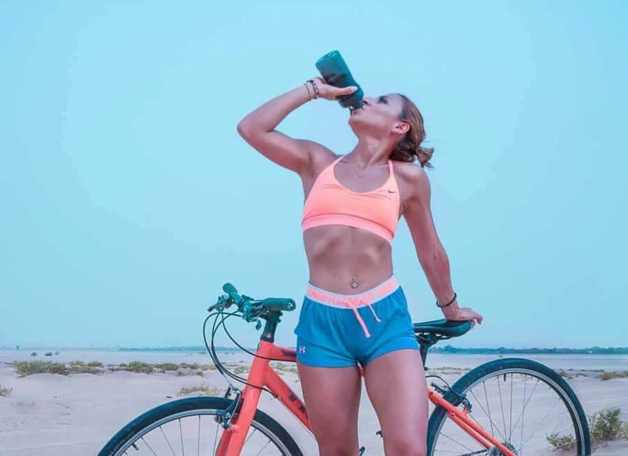 Woman drinking out of a bottle with a bike.