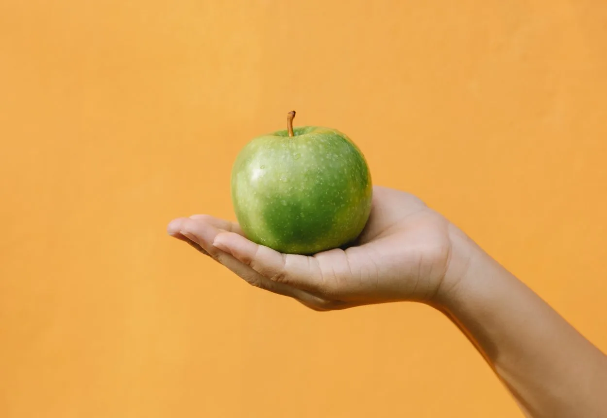 A hand holding up a green apple.
